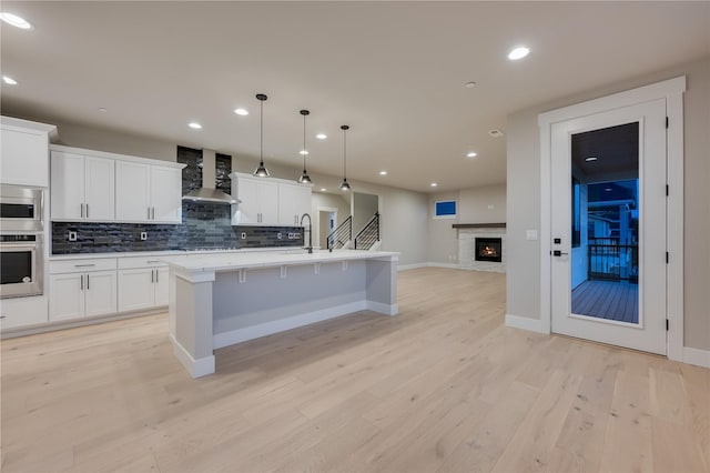 20239 125th Ave NE Unit Sm2-11, Bothell, WA 98011 - kitchen featuring wall chimney range hood, appliances with stainless steel finishes, light wood finished floors, open floor plan, and backsplash