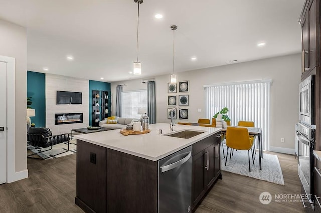 kitchen with dark brown cabinetry, sink, stainless steel appliances, dark hardwood / wood-style floors, and a tiled fireplace