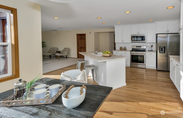 kitchen with white cabinets, stainless steel appliances, light hardwood / wood-style floors, a kitchen island with sink, and a breakfast bar area