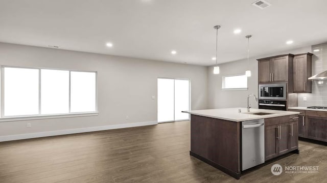 kitchen featuring dark wood-type flooring, tasteful backsplash, an island with sink, pendant lighting, and appliances with stainless steel finishes