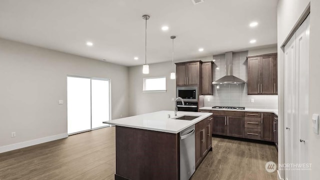 kitchen featuring sink, wall chimney range hood, decorative light fixtures, a kitchen island with sink, and appliances with stainless steel finishes