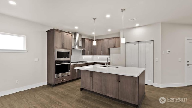 kitchen with stainless steel oven, wall chimney range hood, pendant lighting, black gas cooktop, and an island with sink