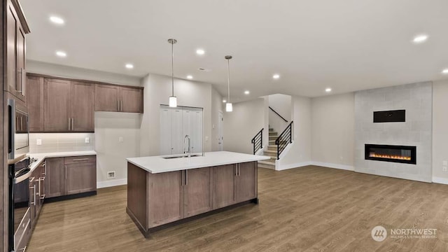 kitchen with a tile fireplace, sink, hanging light fixtures, decorative backsplash, and a kitchen island with sink