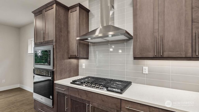 kitchen with wall oven, backsplash, dark brown cabinetry, stainless steel gas cooktop, and wall chimney range hood