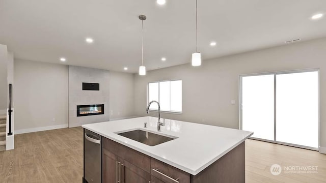 kitchen with a large fireplace, sink, pendant lighting, light hardwood / wood-style floors, and an island with sink