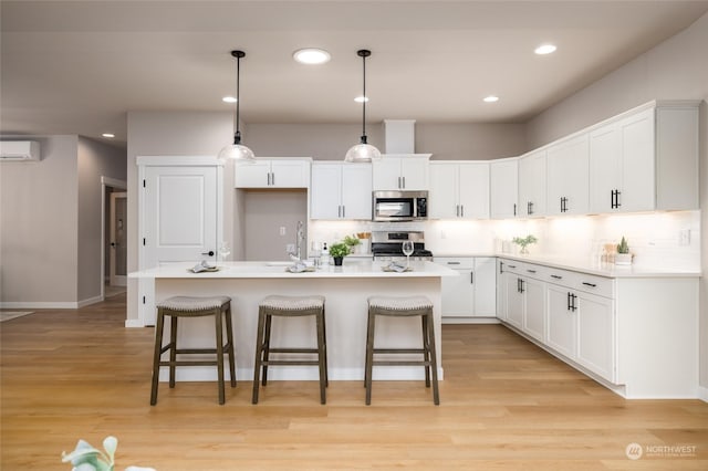 kitchen featuring an AC wall unit, white cabinetry, an island with sink, and stainless steel appliances