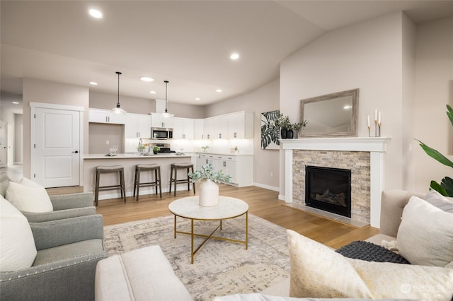 living room with vaulted ceiling, a fireplace, and light hardwood / wood-style flooring