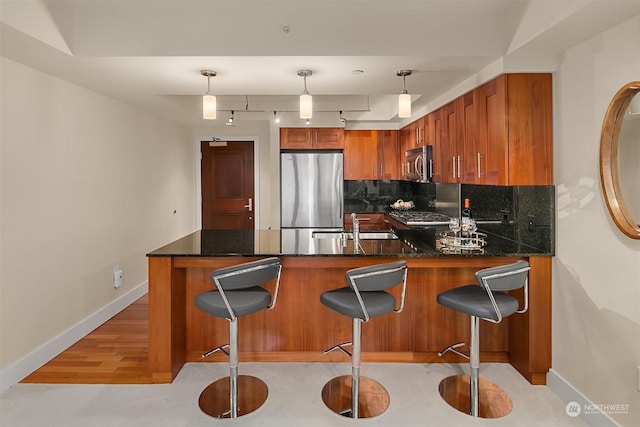 kitchen with kitchen peninsula, appliances with stainless steel finishes, pendant lighting, and tasteful backsplash