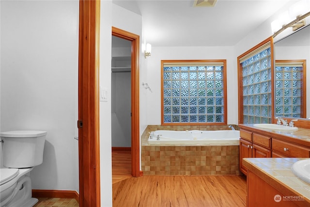 bathroom with tiled tub, hardwood / wood-style flooring, vanity, and toilet