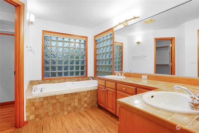 bathroom featuring hardwood / wood-style flooring, vanity, and a relaxing tiled tub