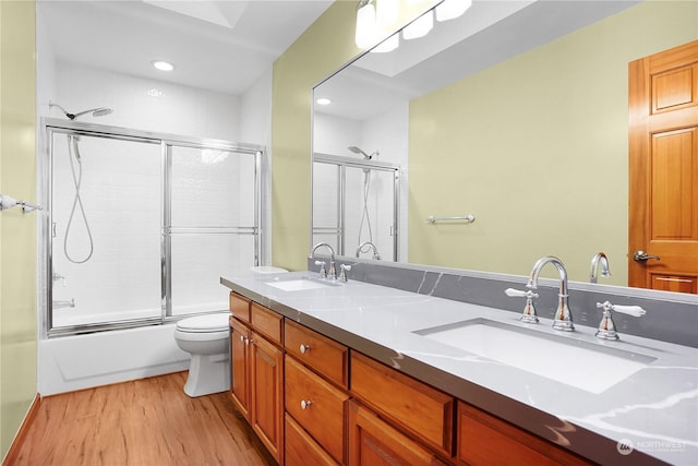 full bathroom featuring shower / bath combination with glass door, hardwood / wood-style floors, vanity, and toilet