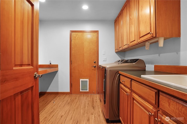 laundry area with washing machine and clothes dryer, cabinets, and light wood-type flooring