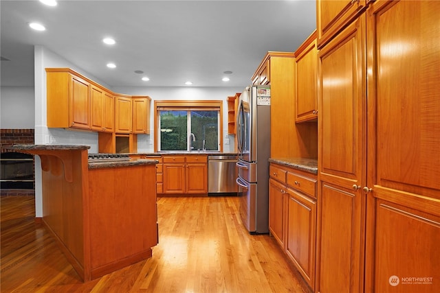 kitchen featuring sink, stainless steel appliances, dark stone countertops, a kitchen bar, and light wood-type flooring