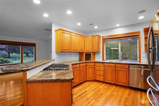 kitchen with sink, stainless steel appliances, kitchen peninsula, dark stone countertops, and light hardwood / wood-style floors