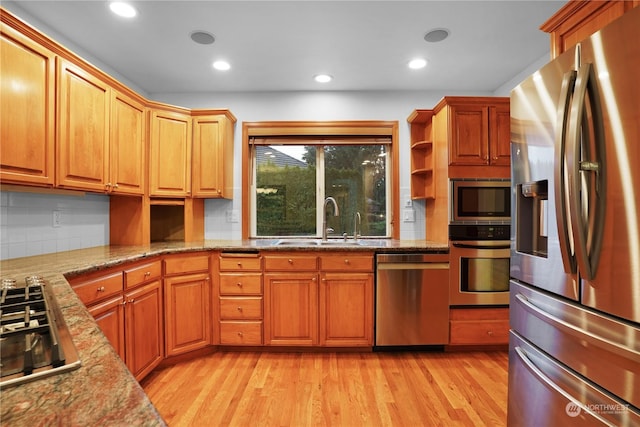 kitchen with light stone countertops, tasteful backsplash, stainless steel appliances, sink, and light hardwood / wood-style flooring