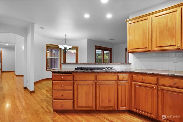 kitchen with stainless steel gas stovetop, light stone countertops, tasteful backsplash, light hardwood / wood-style floors, and a chandelier