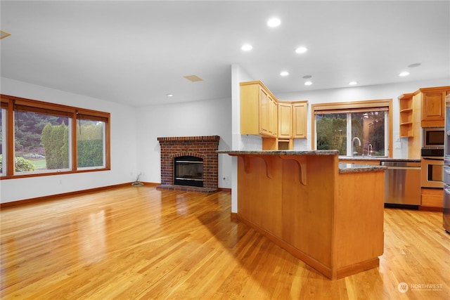 kitchen featuring a kitchen breakfast bar, a brick fireplace, light wood-type flooring, appliances with stainless steel finishes, and a healthy amount of sunlight