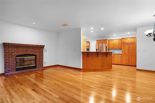 unfurnished living room with light hardwood / wood-style floors, a notable chandelier, and a brick fireplace