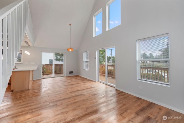 unfurnished living room featuring light wood-type flooring, a towering ceiling, and plenty of natural light