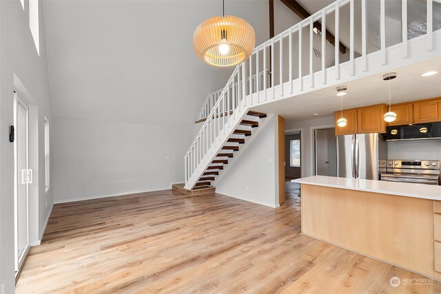 kitchen with decorative light fixtures, a towering ceiling, stainless steel appliances, and light hardwood / wood-style flooring