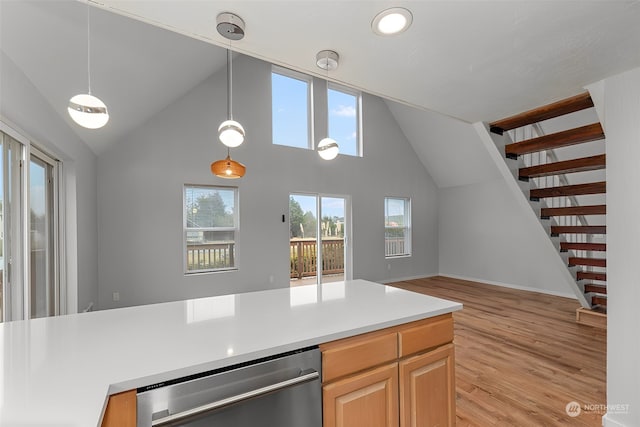 kitchen with pendant lighting, stainless steel dishwasher, light wood-type flooring, a towering ceiling, and light brown cabinetry