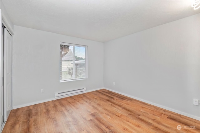 unfurnished room with baseboard heating and light hardwood / wood-style floors