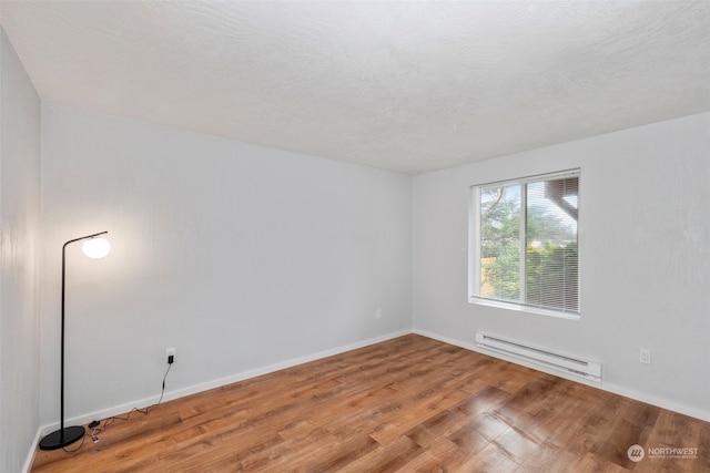 empty room with a textured ceiling, wood-type flooring, and baseboard heating