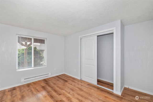 unfurnished bedroom featuring light hardwood / wood-style floors, a closet, and a baseboard heating unit