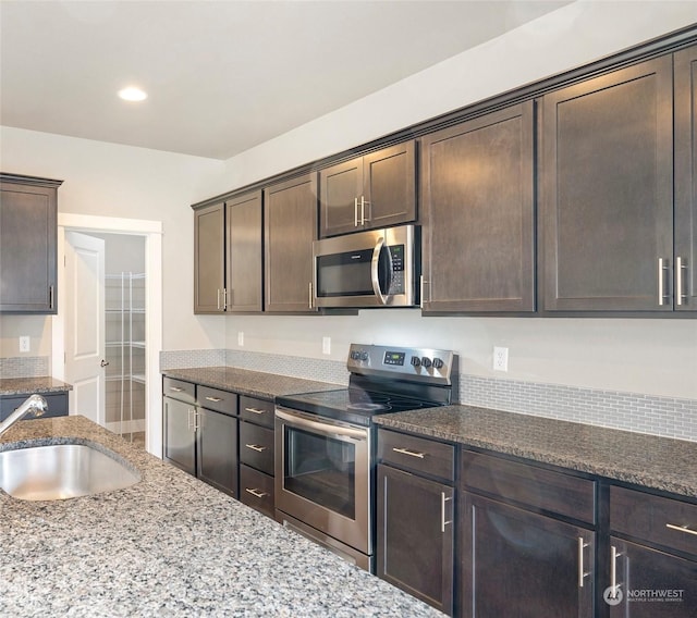 kitchen featuring stone counters, appliances with stainless steel finishes, sink, and dark brown cabinetry