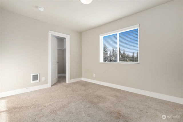 unfurnished bedroom with a walk in closet and light carpet