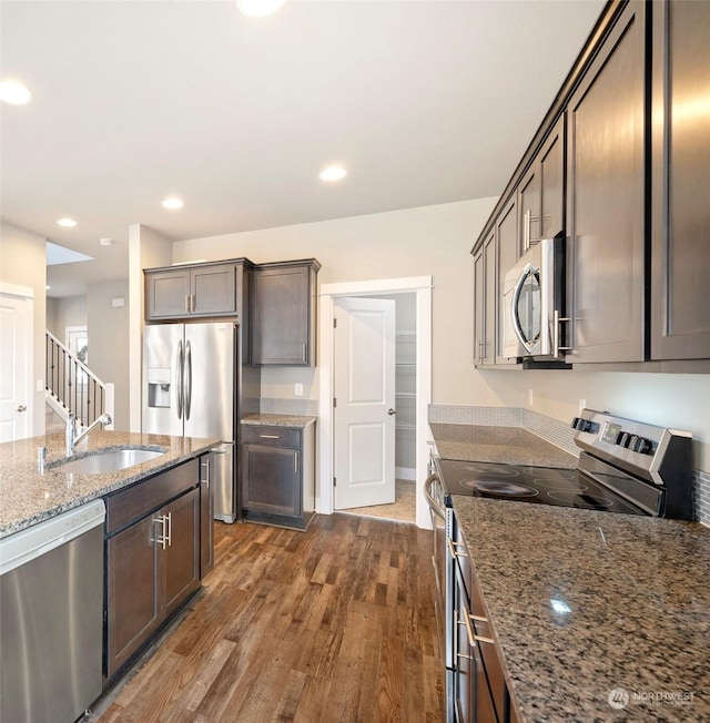 kitchen with sink, appliances with stainless steel finishes, dark brown cabinetry, stone countertops, and dark hardwood / wood-style flooring