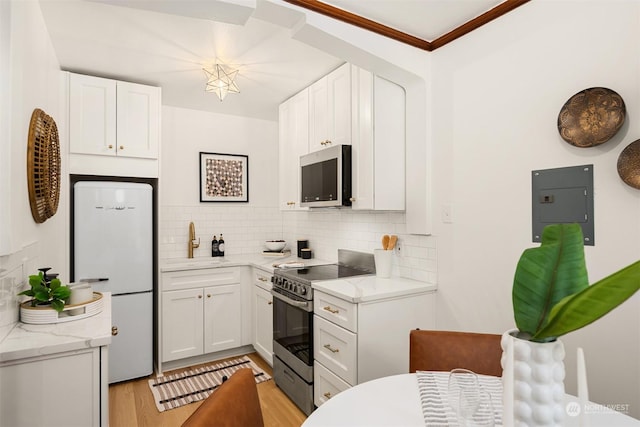 kitchen with white cabinets, decorative backsplash, appliances with stainless steel finishes, and light hardwood / wood-style flooring