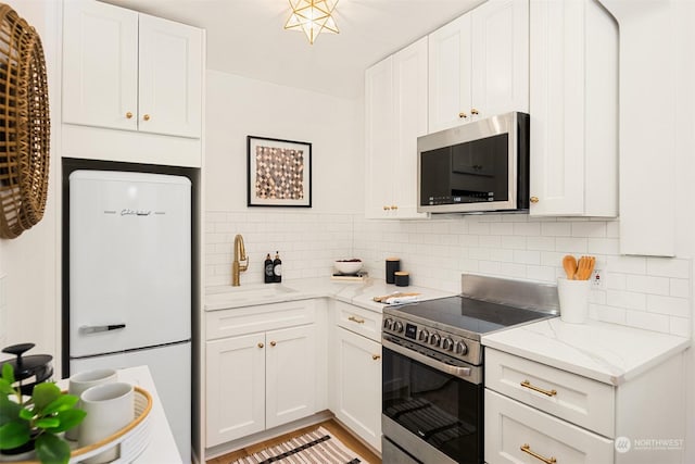 kitchen with light stone countertops, backsplash, stainless steel appliances, sink, and white cabinets