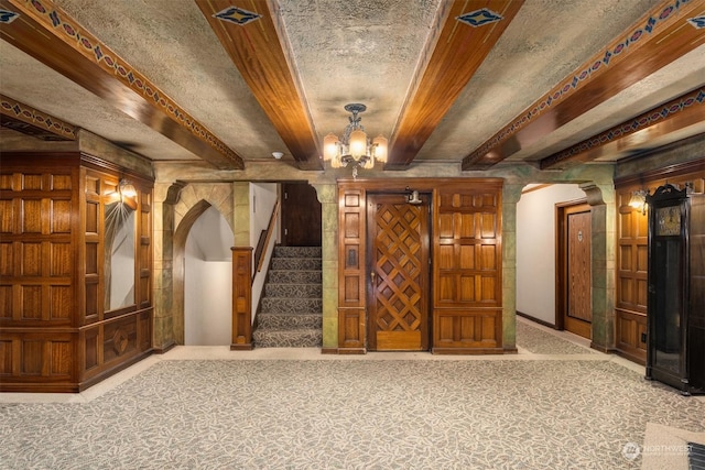 interior space with beam ceiling, decorative columns, a textured ceiling, and a notable chandelier