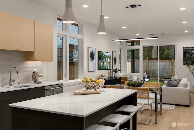 kitchen featuring light brown cabinets, sink, light stone countertops, decorative light fixtures, and a kitchen island