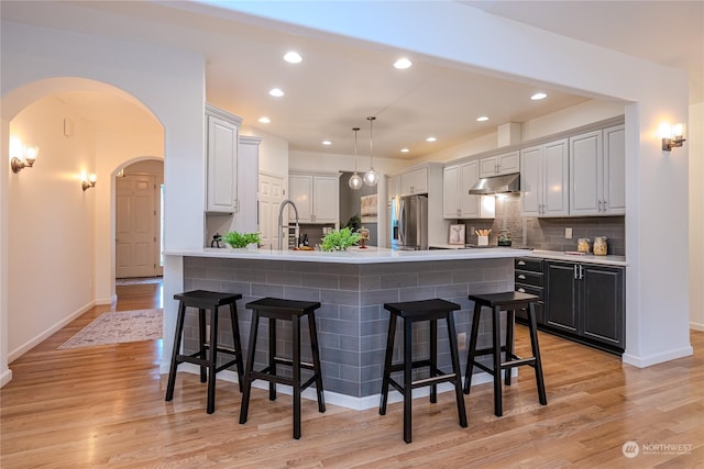 kitchen with hanging light fixtures, stainless steel fridge with ice dispenser, tasteful backsplash, light wood-type flooring, and a breakfast bar area