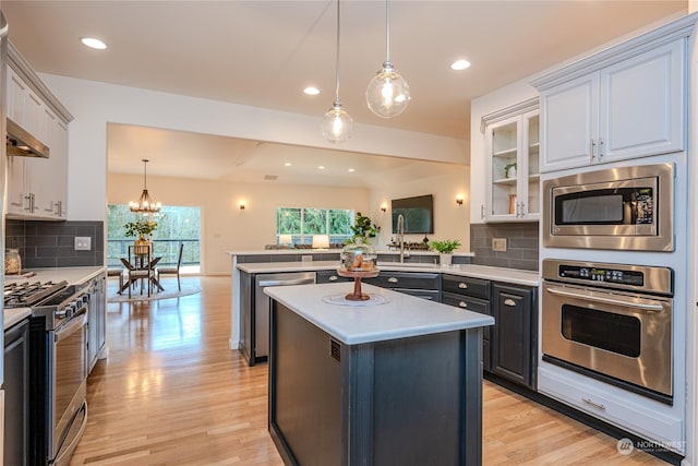 kitchen with appliances with stainless steel finishes, a center island, white cabinetry, decorative light fixtures, and tasteful backsplash