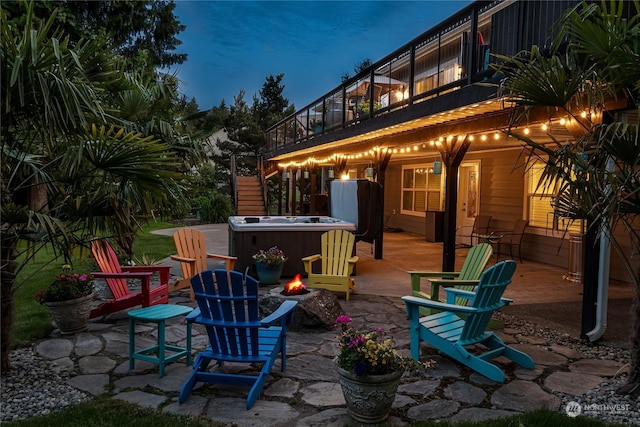 patio terrace at dusk featuring a hot tub, a fire pit, and a balcony