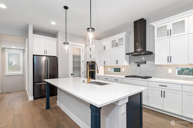 kitchen featuring white cabinetry, a center island with sink, stainless steel appliances, and wall chimney range hood