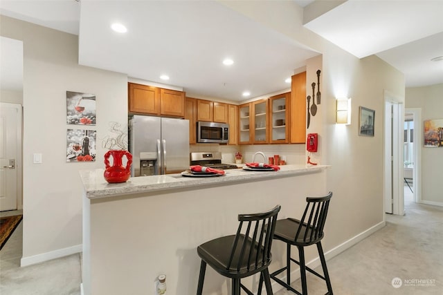 kitchen with kitchen peninsula, a breakfast bar, light colored carpet, and stainless steel appliances