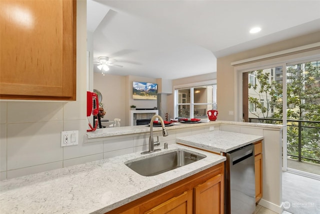 kitchen featuring light stone countertops, sink, ceiling fan, stainless steel dishwasher, and a tiled fireplace