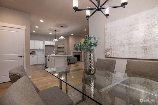 dining space with a stone fireplace, a chandelier, vaulted ceiling, and light wood-type flooring