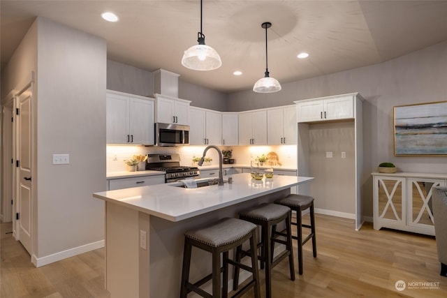 kitchen featuring appliances with stainless steel finishes, a kitchen island with sink, sink, white cabinetry, and hanging light fixtures