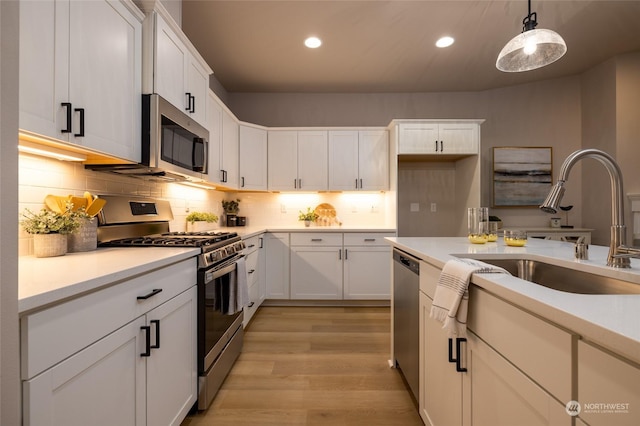 kitchen featuring backsplash, stainless steel appliances, light hardwood / wood-style floors, white cabinetry, and hanging light fixtures