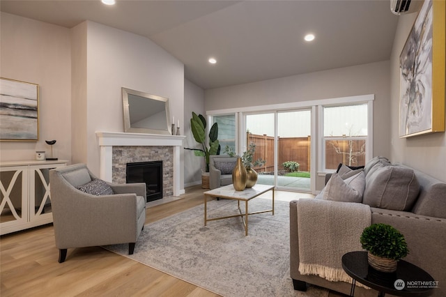 living room with a stone fireplace, a wall mounted AC, vaulted ceiling, and light wood-type flooring