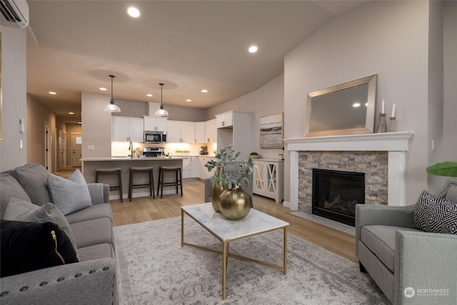 living room with a wall mounted air conditioner, light wood-type flooring, a fireplace, and vaulted ceiling