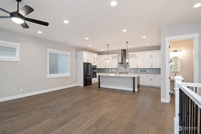 kitchen featuring wall chimney exhaust hood, backsplash, decorative light fixtures, a center island with sink, and white cabinets