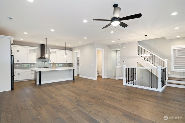 kitchen with pendant lighting, an island with sink, fridge, and wall chimney range hood