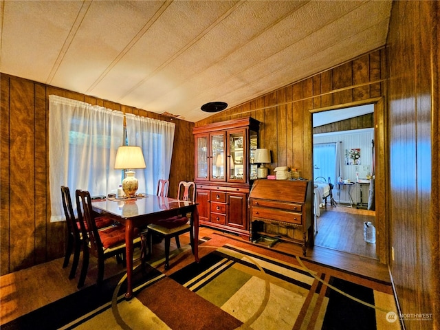 dining space featuring wood walls, a textured ceiling, and vaulted ceiling