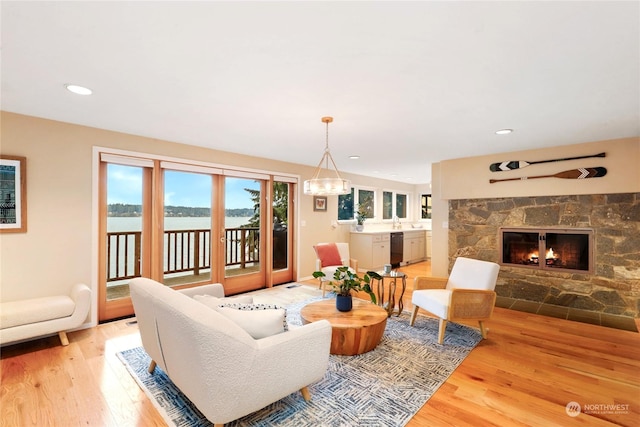 living room featuring an inviting chandelier, a water view, a stone fireplace, and light wood-type flooring